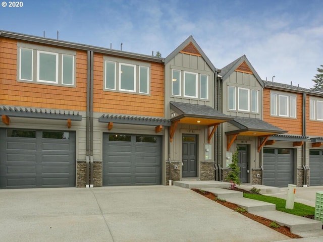 view of property featuring a garage, driveway, board and batten siding, and stone siding