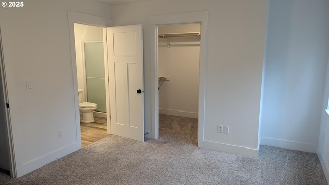 unfurnished bedroom featuring light carpet, a closet, a walk in closet, and baseboards