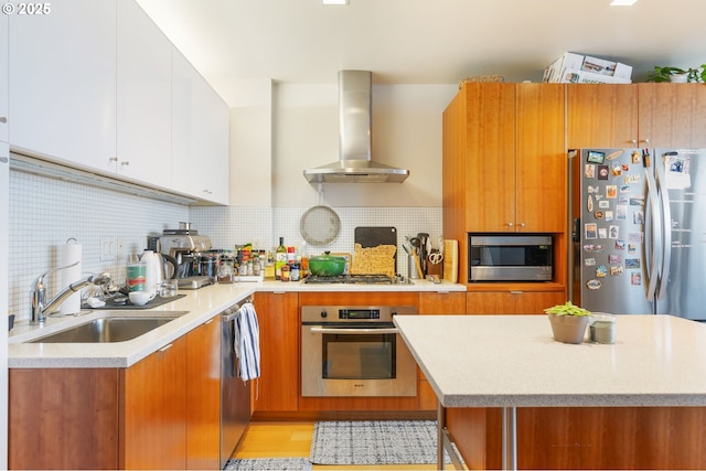 kitchen featuring a sink, wall chimney exhaust hood, brown cabinets, and appliances with stainless steel finishes