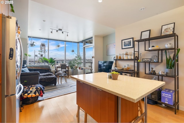 kitchen featuring freestanding refrigerator, rail lighting, light wood-type flooring, light stone countertops, and floor to ceiling windows