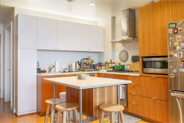 kitchen with a breakfast bar, decorative backsplash, wall chimney exhaust hood, light countertops, and appliances with stainless steel finishes