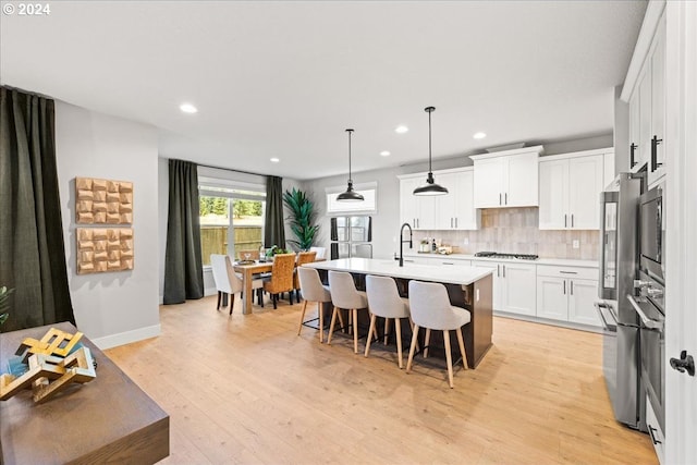 kitchen with appliances with stainless steel finishes, backsplash, pendant lighting, a center island with sink, and white cabinets