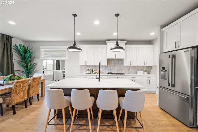 kitchen featuring decorative backsplash, appliances with stainless steel finishes, a kitchen island with sink, pendant lighting, and white cabinets