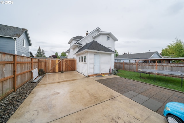 back of property with a trampoline, a patio, a gate, concrete driveway, and a shingled roof