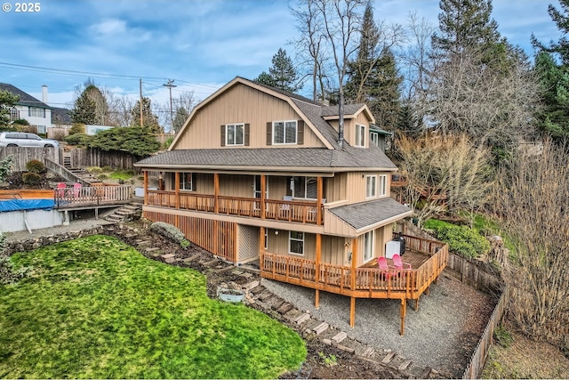 rear view of house featuring roof with shingles, fence, a deck, and a yard