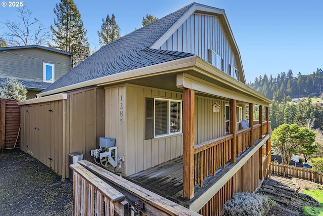 view of side of home featuring a shingled roof, board and batten siding, a chimney, and fence