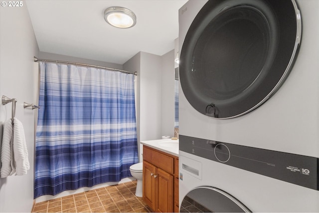 bathroom featuring a shower with curtain, vanity, stacked washer / drying machine, and toilet