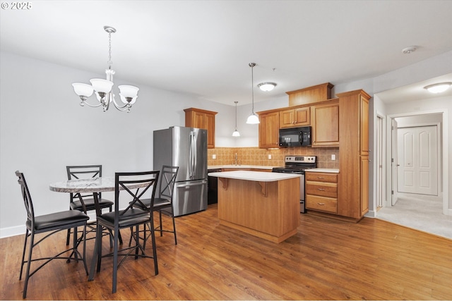 kitchen with pendant lighting, appliances with stainless steel finishes, hardwood / wood-style floors, a center island, and decorative backsplash