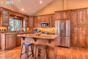 kitchen with stainless steel appliances, brown cabinetry, a kitchen island, and light wood-style floors