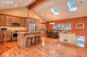 kitchen featuring light wood-style flooring, appliances with stainless steel finishes, brown cabinets, and a kitchen breakfast bar