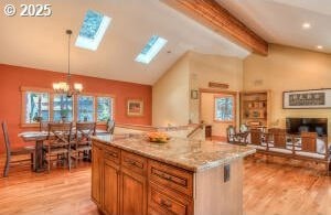 kitchen featuring light stone countertops, a notable chandelier, light wood-style floors, brown cabinets, and lofted ceiling with skylight