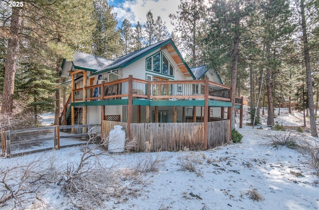 snow covered back of property featuring a garage, fence, and a wooden deck