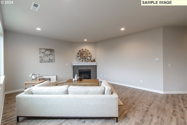 living room with recessed lighting, visible vents, wood finished floors, and a tiled fireplace