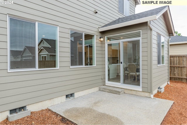 property entrance with a patio area, roof with shingles, and fence