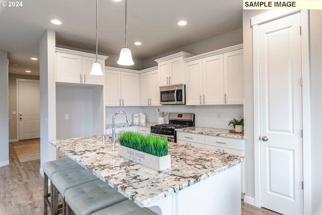 kitchen with light stone countertops, light wood finished floors, white cabinets, appliances with stainless steel finishes, and tasteful backsplash