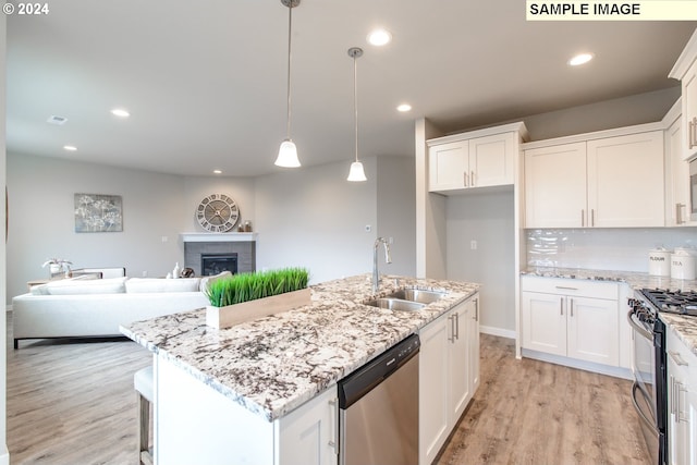 kitchen featuring open floor plan, light wood-type flooring, appliances with stainless steel finishes, a fireplace, and a sink