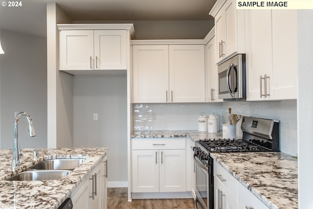 kitchen featuring a sink, light stone counters, tasteful backsplash, stainless steel appliances, and white cabinets