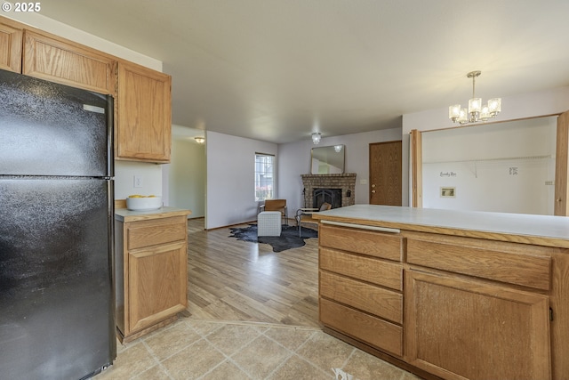 kitchen with an inviting chandelier, a brick fireplace, light countertops, freestanding refrigerator, and decorative light fixtures