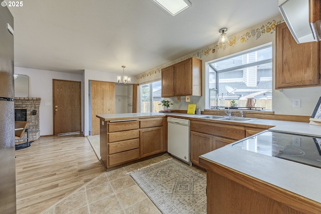 kitchen featuring white dishwasher, brown cabinetry, a peninsula, and a sink