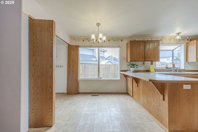 kitchen with a notable chandelier, a breakfast bar area, light countertops, brown cabinetry, and visible vents