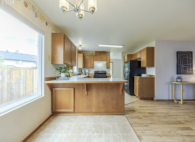 kitchen with freestanding refrigerator, a peninsula, light countertops, electric range oven, and a chandelier