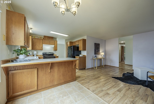 kitchen with a notable chandelier, light countertops, brown cabinetry, a peninsula, and black appliances