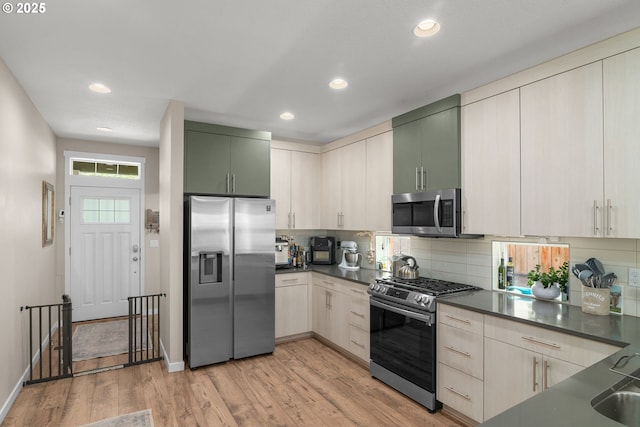 6910 SE Lamphier St, Milwaukie, OR 97222 - kitchen featuring appliances with stainless steel finishes, dark countertops, backsplash, light wood-style floors, and recessed lighting