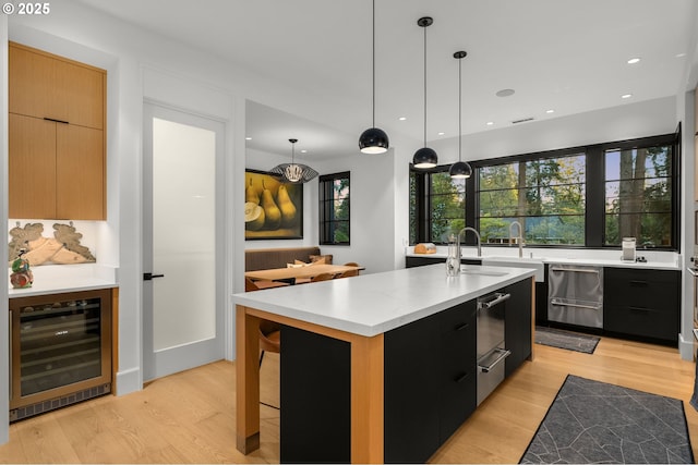 1235 Andrews Rd, Lake Oswego, OR 97034 - kitchen featuring beverage cooler, modern cabinets, dark cabinets, an island with sink, and light wood finished floors