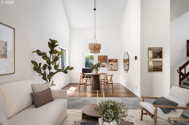 living area featuring stairway, high vaulted ceiling, wood finished floors, and a notable chandelier