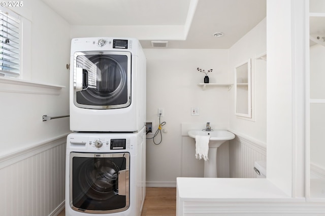 bathroom with visible vents, stacked washer and dryer, wood finished floors, a wainscoted wall, and a sink