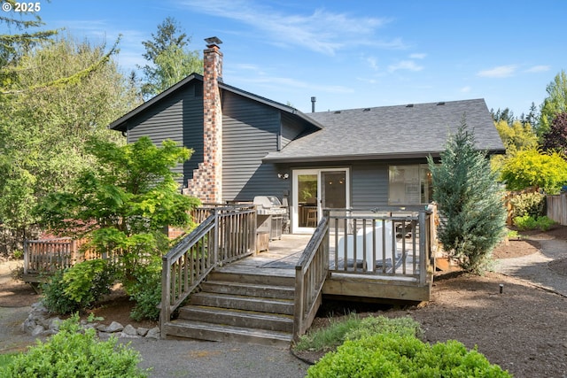 rear view of house featuring a shingled roof, a wooden deck, and a chimney