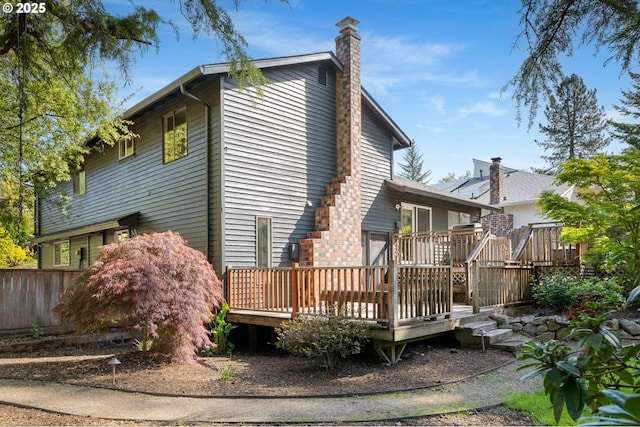 rear view of house featuring a deck, fence, and a chimney