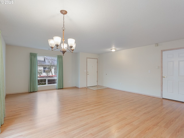 spare room with a chandelier, light wood-style flooring, and baseboards