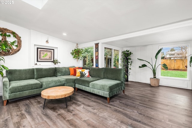 living room featuring a skylight, plenty of natural light, wood finished floors, and a decorative wall