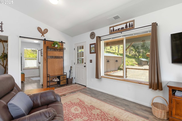 living area with visible vents, wood finished floors, baseboards, a barn door, and vaulted ceiling