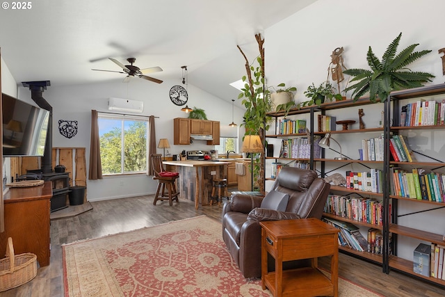 living room with a wood stove, wood finished floors, lofted ceiling, a wall unit AC, and a ceiling fan