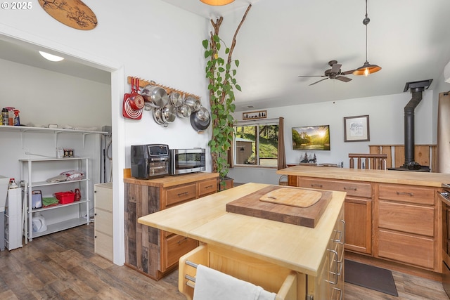 kitchen featuring a wood stove, butcher block counters, dark wood-type flooring, stainless steel microwave, and a ceiling fan