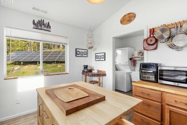 kitchen featuring stacked washer / dryer, visible vents, light wood-type flooring, butcher block counters, and lofted ceiling