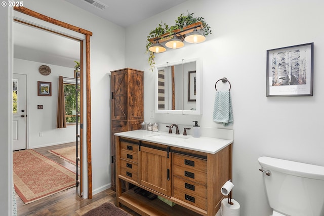 bathroom featuring vanity, visible vents, wood finished floors, toilet, and baseboards