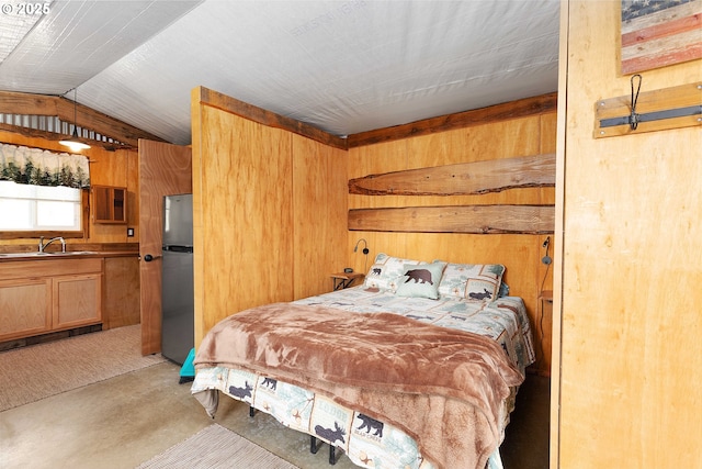 bedroom featuring concrete flooring, a sink, wood walls, freestanding refrigerator, and lofted ceiling