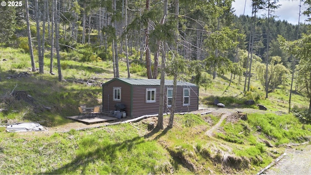 view of side of property with a wooden deck, metal roof, and a wooded view