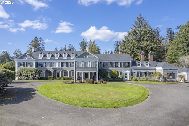 shingle-style home featuring a chimney, curved driveway, and a front yard