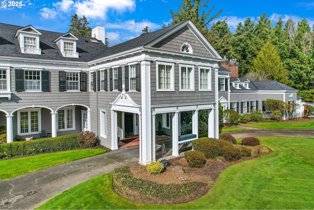 view of front of house with driveway, a chimney, and a front lawn