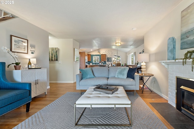 living area with vaulted ceiling, a brick fireplace, wood finished floors, and baseboards