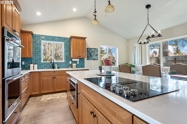 kitchen featuring a sink, stainless steel double oven, light countertops, black electric stovetop, and hanging light fixtures