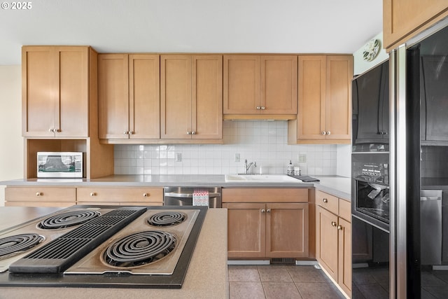 kitchen featuring appliances with stainless steel finishes, a sink, decorative backsplash, light tile patterned floors, and light countertops