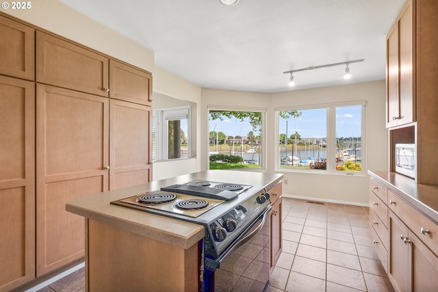 kitchen featuring black electric range, light tile patterned flooring, a water view, a center island, and light countertops