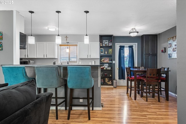 1701 Walnut St, La Grande, OR 97850 - kitchen with a breakfast bar, white cabinets, light wood-type flooring, pendant lighting, and a peninsula