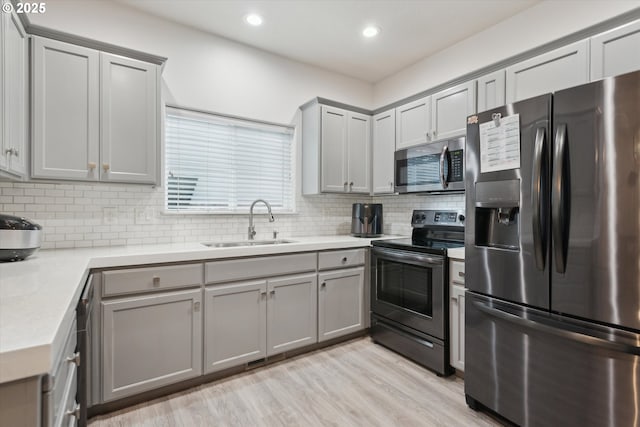 kitchen with light wood-type flooring, decorative backsplash, gray cabinets, appliances with stainless steel finishes, and a sink