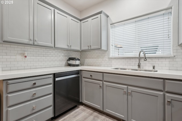 kitchen featuring a sink, stainless steel dishwasher, gray cabinetry, and light countertops